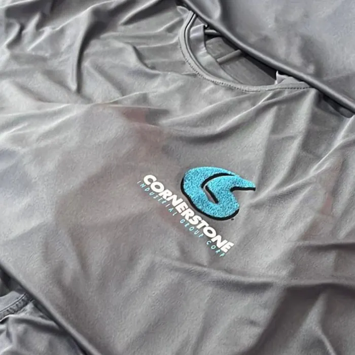 Camisa gris de tela de rendimiento con el logo de la empresa bordado en azul en el pecho