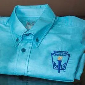 Camisa turquesa doblada con el emblema de una sociedad de honor estudiantil bordado