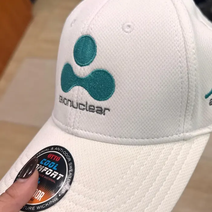 Gorra blanca nueva con el logo de una empresa de servicios nucleares bordado en verde azulado