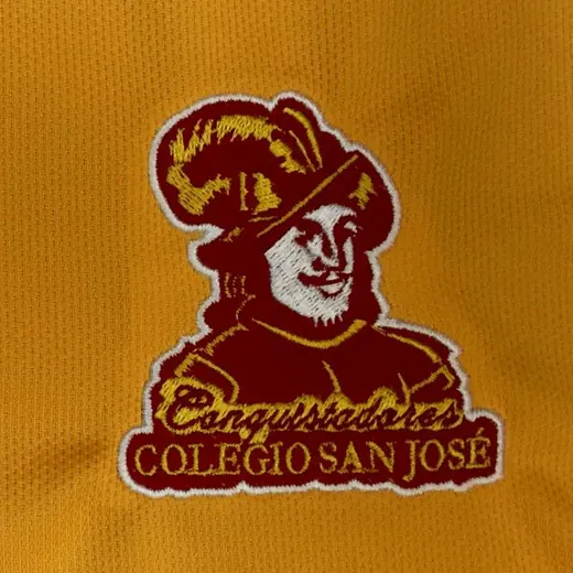 Escudo institucional bordado sobre un polo escolar dorado